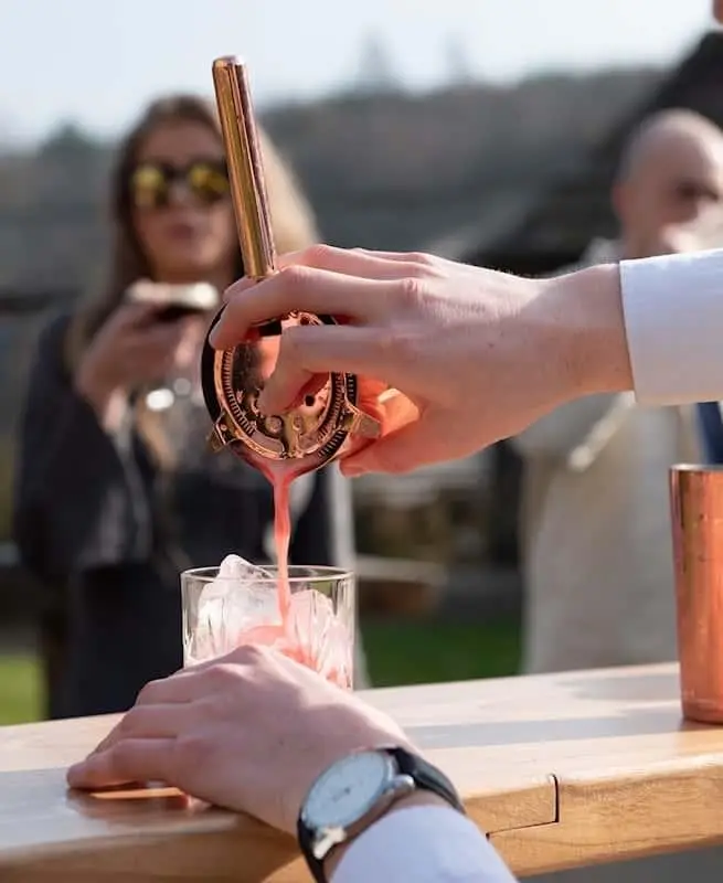 Bartender pouring a cocktail from a copper jigger at an outdoor event