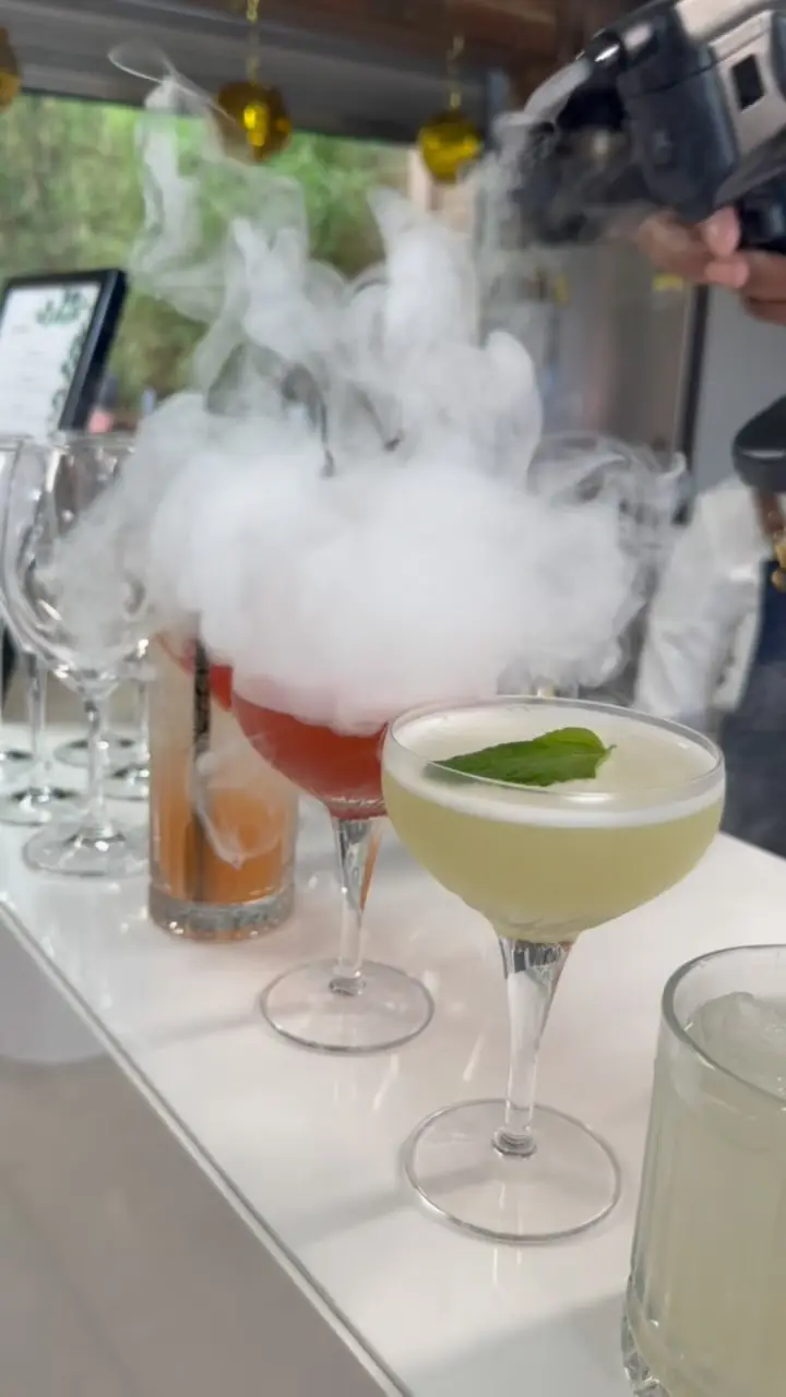 A smoking red cocktail and a pale green cocktail with mint on a party bar