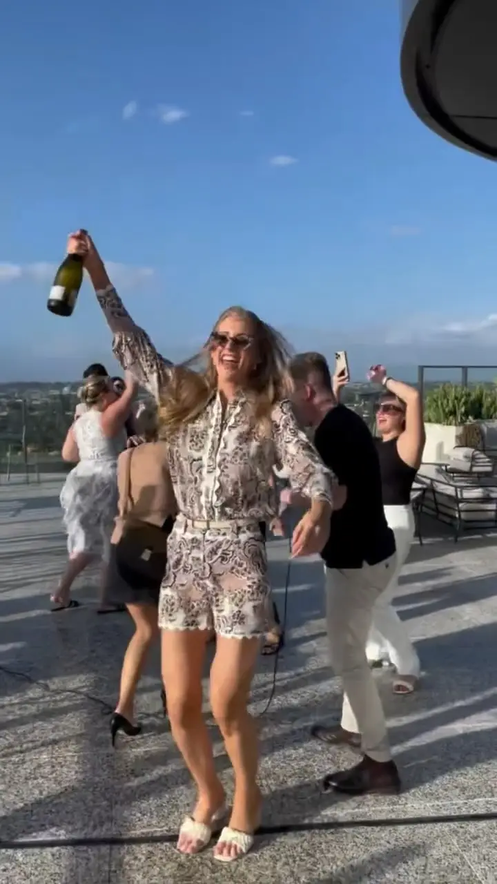 Guests celebrating on a rooftop terrace at a Christmas party, one holding a bottle of champagne aloft