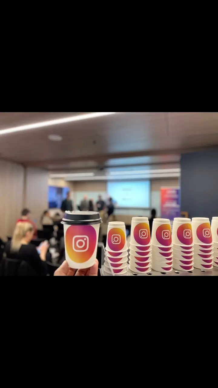 Branded Instagram coffee cups lined up at a conference, with the audience behind