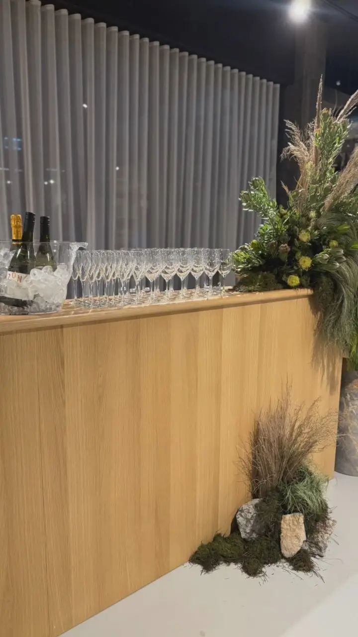 A timber bar with rows of champagne flutes and native flowers at a corporate function