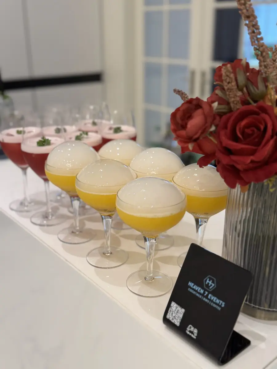 Foam-topped signature cocktails lined up on a Heaven 7 Events bar beside red roses