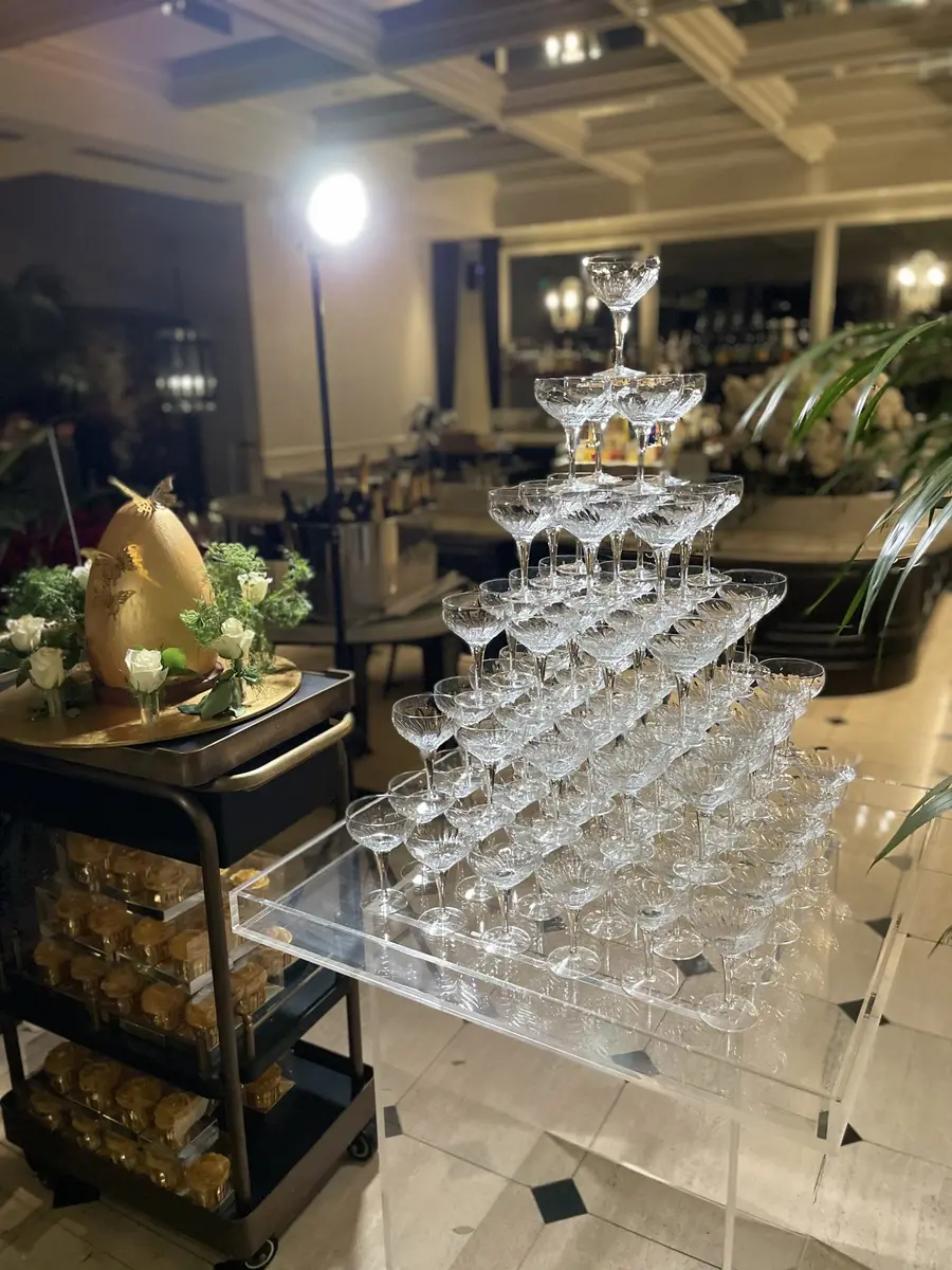 Champagne tower of coupe glasses beside a dessert cart at an evening event